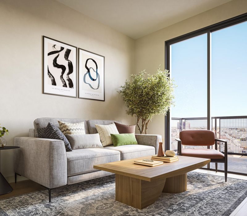 Modern living room with a gray sofa, coffee table, armchair, art prints, and large window overlooking a city.