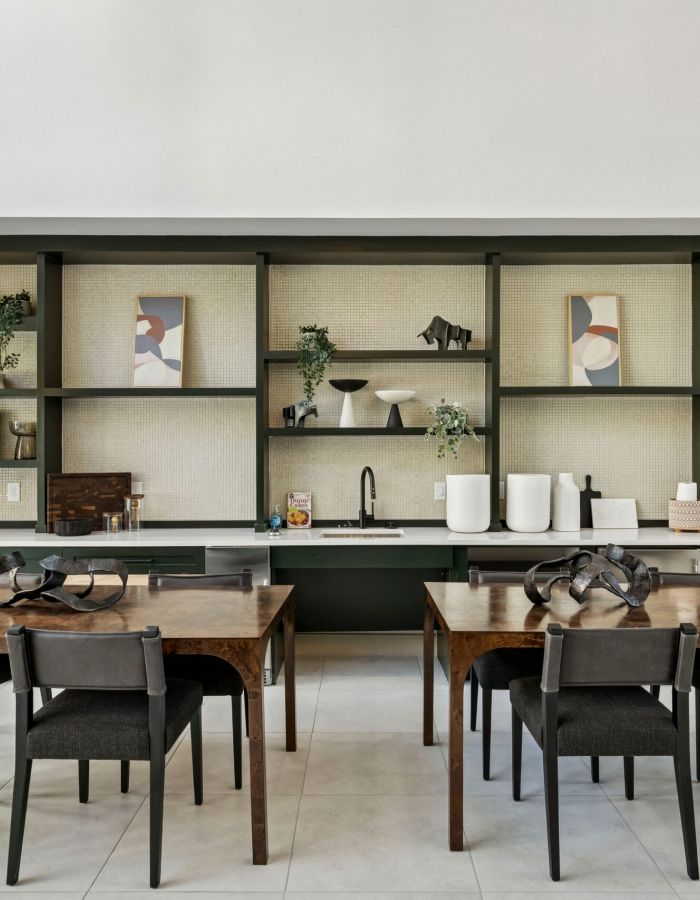 Modern kitchen and dining area with wooden tables, dark chairs, open shelves, and decorative plants.