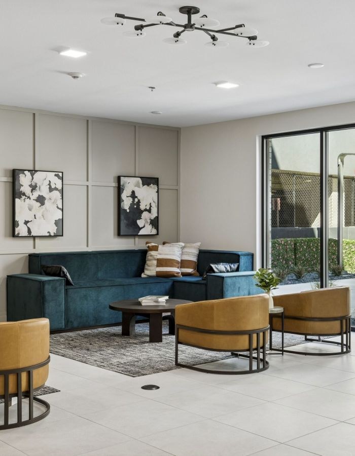 Modern lounge with tan chairs, a teal sofa, abstract art, and large window letting in natural light.