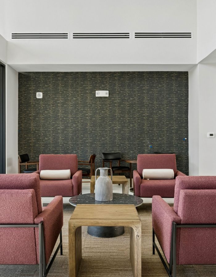 Modern lounge area with four red armchairs, a wooden coffee table, and a dark accent wall in the background.