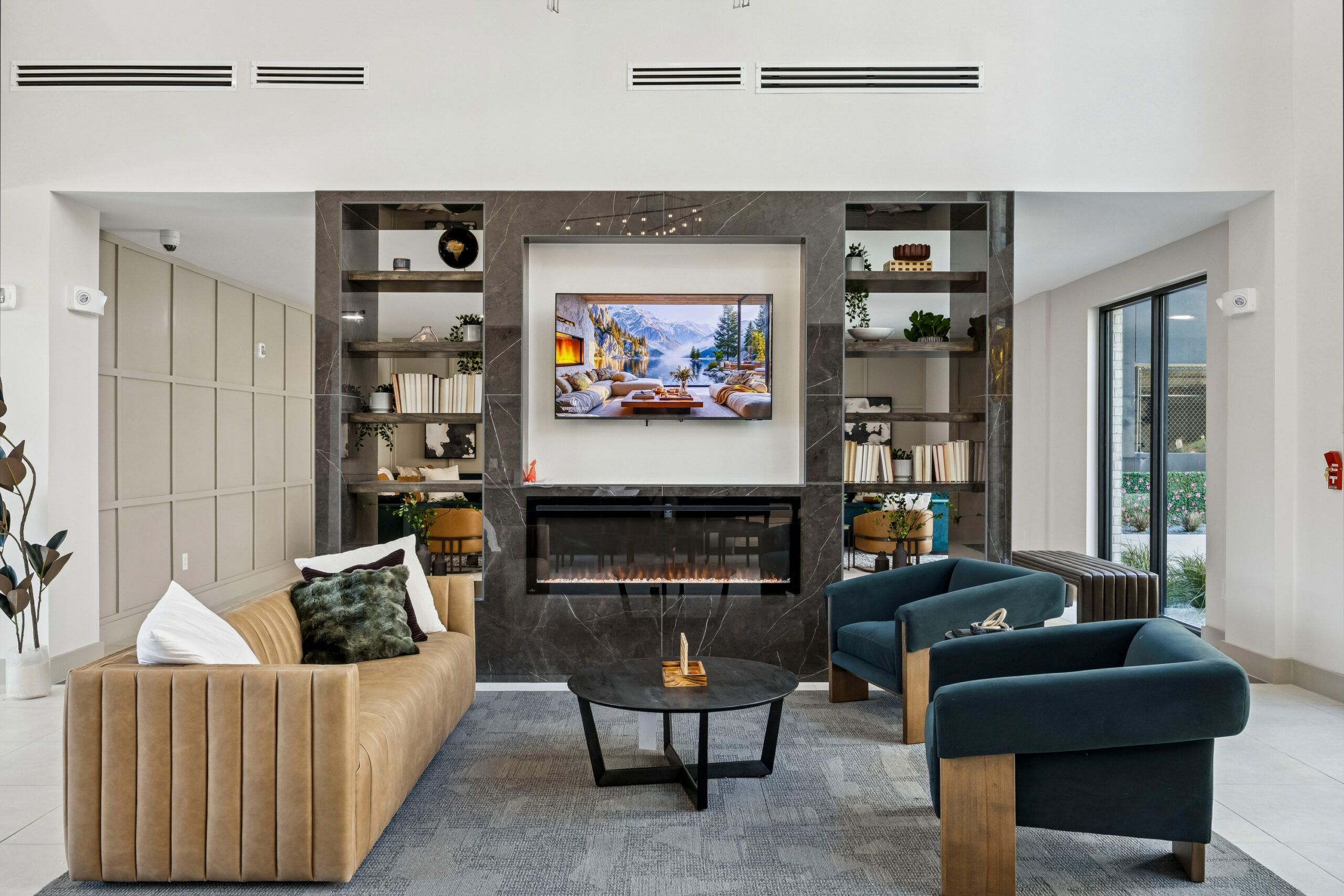 Modern living room with tan sofa, two blue chairs, a fireplace, TV, and built-in shelves with decor and books.