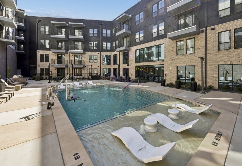 Modern apartment courtyard with a pool, sun loungers in the water, and surrounding seating areas.