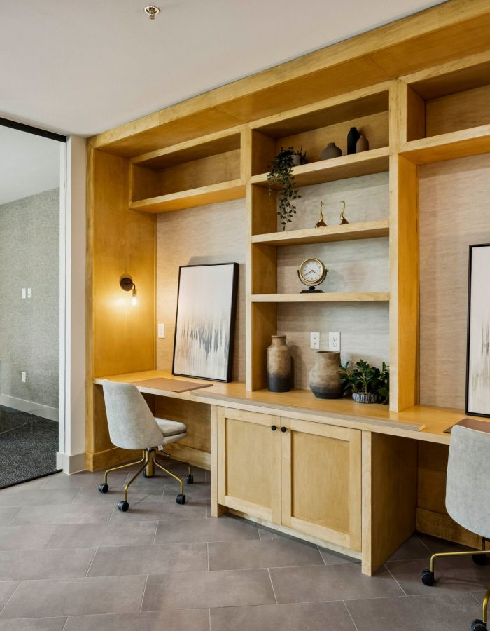 Modern office space with two workstations, light wood shelves, art prints, and gray chairs.