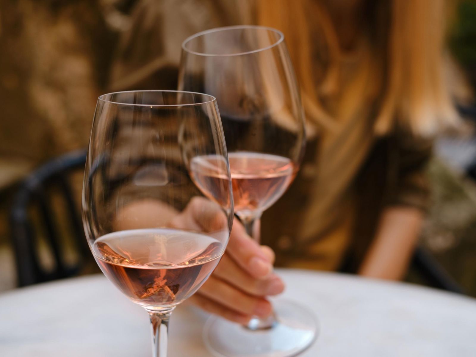 Two glasses of rosé wine on a table, with a person holding one glass in an outdoor setting.