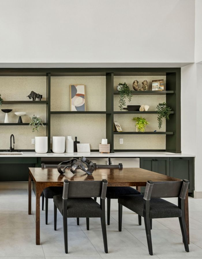 Modern kitchen and dining area with wooden tables, dark chairs, open shelves, and decorative plants.