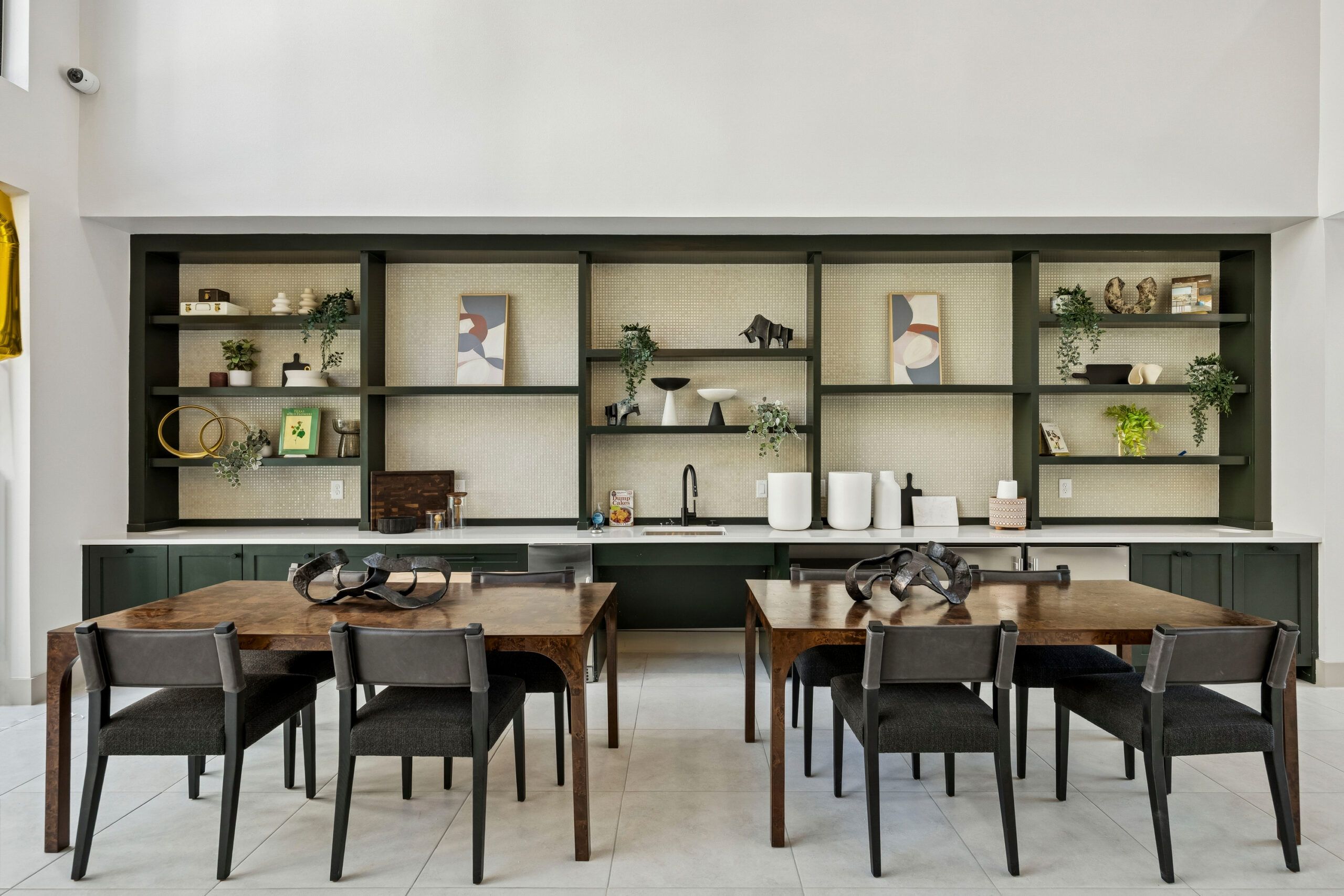 Modern kitchen and dining area with wooden tables, dark chairs, open shelves, and decorative plants.