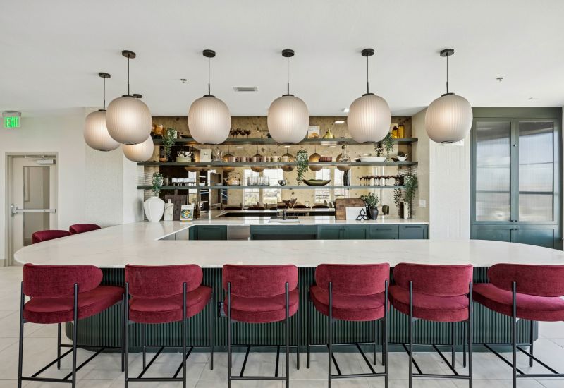 Modern kitchen with a white island, red barstools, pendant lights, and open shelves with decor.