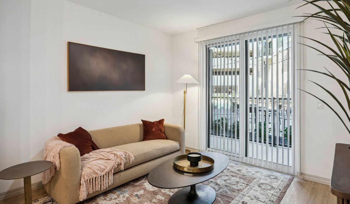 Modern living room with beige sofa, coffee table, floor lamp, and vertical blinds letting in natural light.