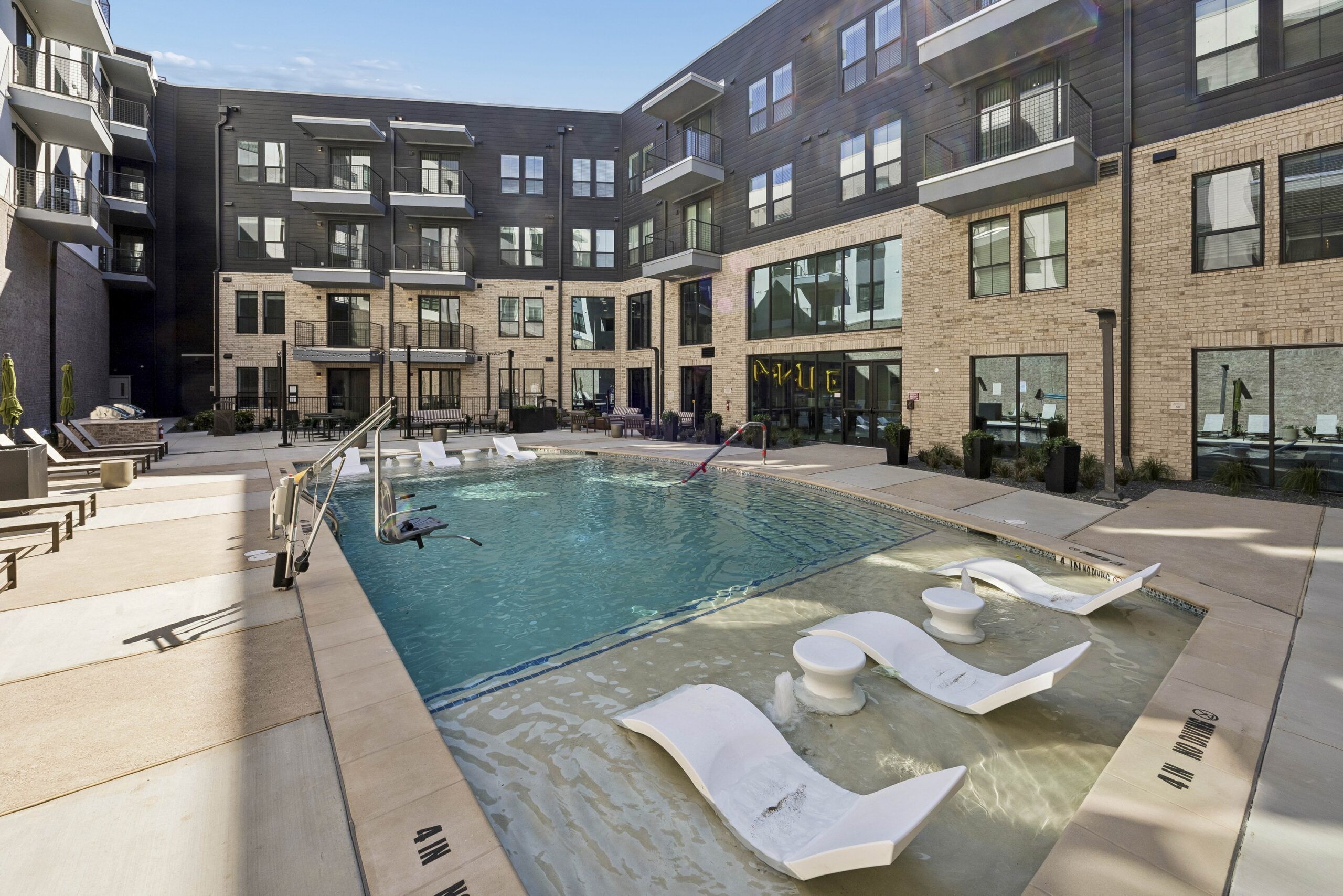 Modern apartment courtyard with a pool, sun loungers in the water, and surrounding seating areas.