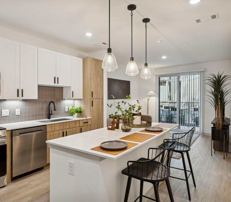 Modern kitchen with island seating, pendant lights, and stainless steel appliances in bright, open space.