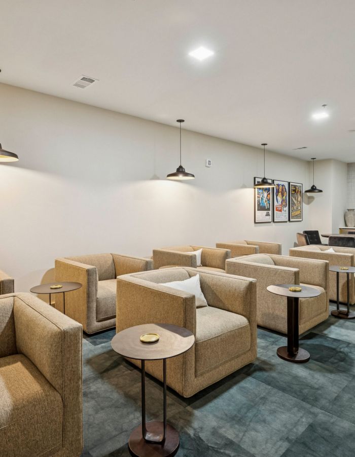 Modern lounge with beige armchairs, small tables, pendant lights, and a workspace at the back.